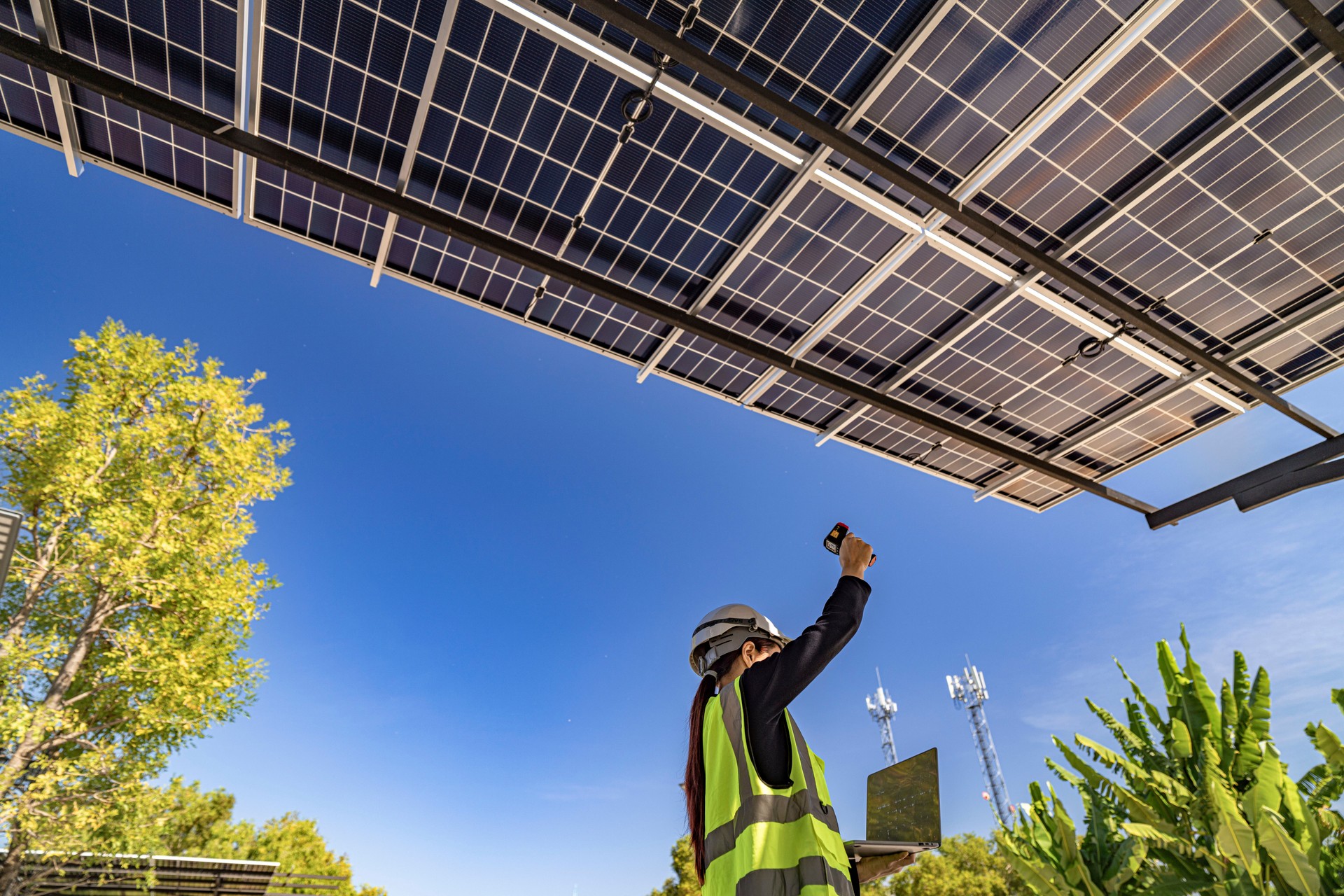 engineer inspecting solar panel installation on a modern structure, pointing to details while holding a laptop, highlighting sustainable energy solutions, efficient design, and renewable innovation.